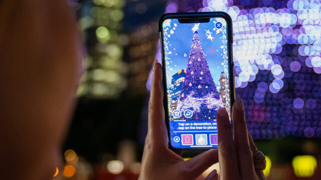 A close up of a phone screen, showing a Christmas tree being augmented with overlaid decorations