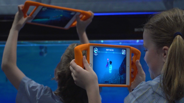 Two children holding up tablets in Positure handled cases, playing a diving game